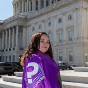 Lupus warrior Karen Miller stands with a purple lupus cape in front of the US capitol building